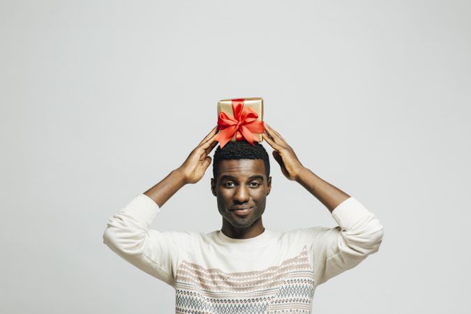 Smiling Black man holding present wrapped in gold and red above his head