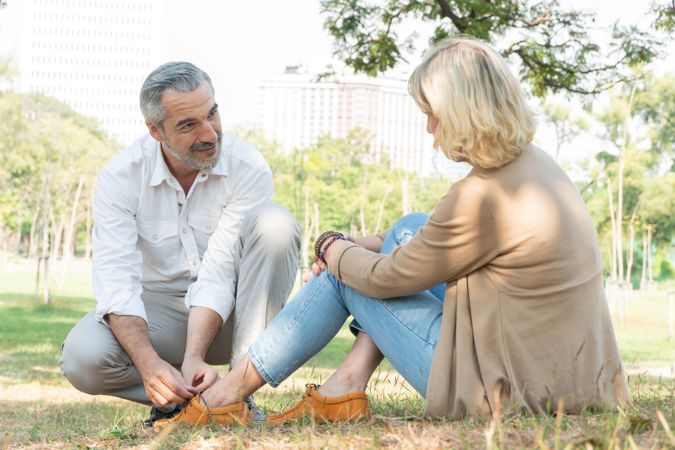Kind mature man tying shoe of woman in park