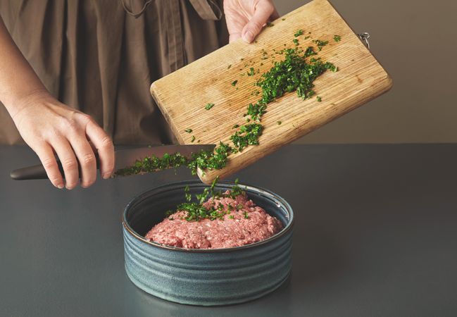 Woman mixing parsley into ground beef