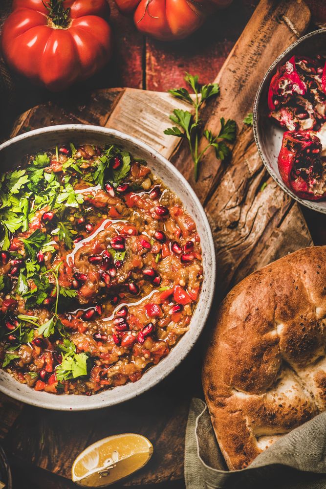 Eggplant dip with pomegranate and parsley garnish on wooden surface