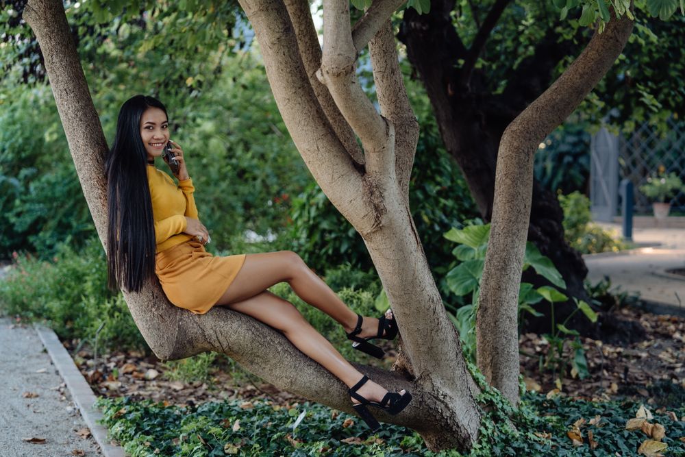 long haired Asian woman sitting on trunk of tree
