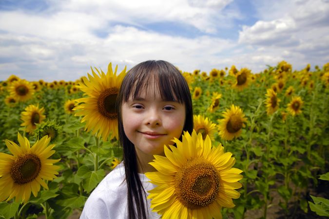 Portrait of child standing next to a sunflower on a cloudy day