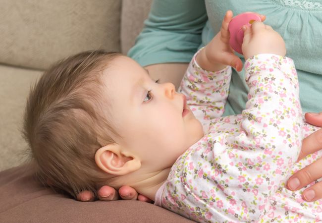 Side view of cute baby playing with pacifier, vertical