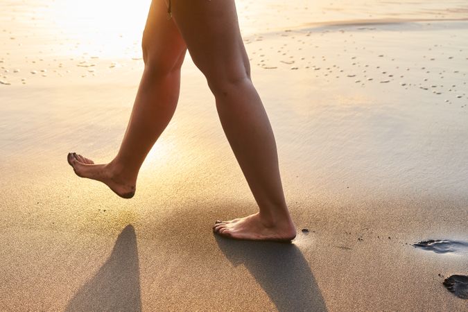 Crop woman strolling on sand of beach
