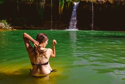 Anonymous woman touching hair and looking at waterfall