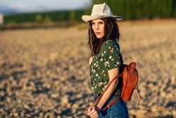 Female in field wearing floral shirt, backpack and straw hat