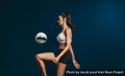 Woman soccer player juggling a ball with her knee against dark background 5XYpo4