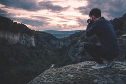 man with photo camera sitting on hill mountain with magnificent sunset