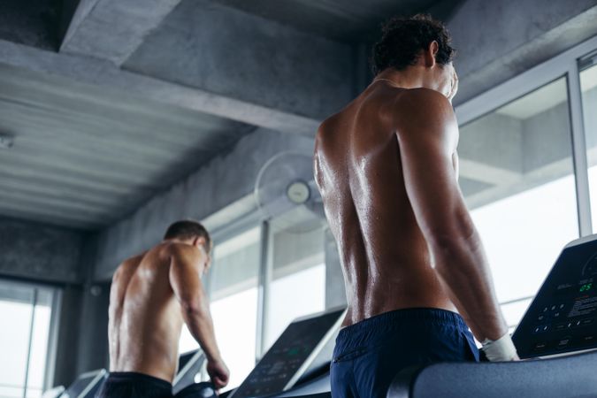 Back of two men standing on treadmill in gym