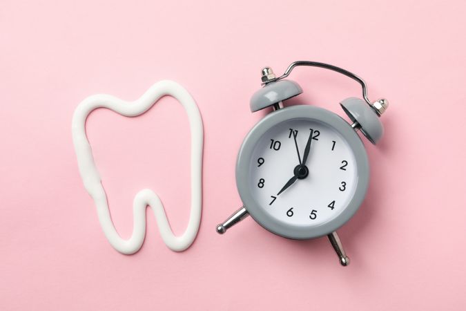 Tooth made of toothpaste and clock on pink background, top view