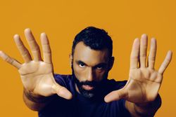 Serious Black man in yellow studio with hands outstretched towards the camera