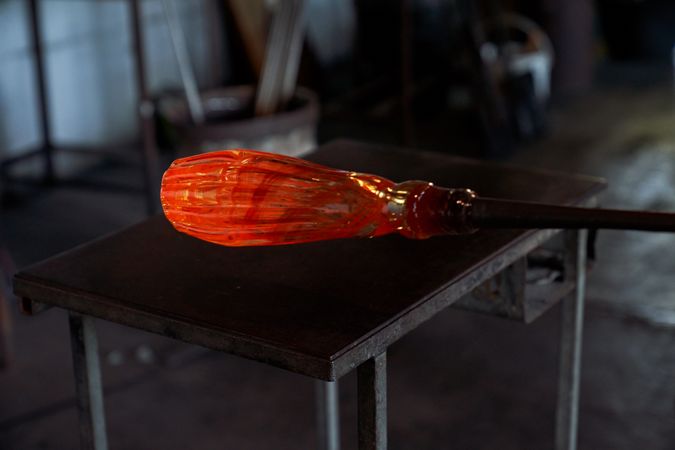 Hot glass on blowpipe against table in dim light