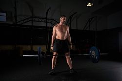 Muscular strong man preparing for lifting barbell with weights