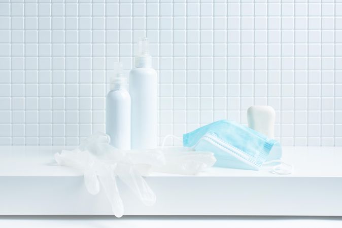 Protective facemask, latex gloves and bottle of soap on tiled bathroom counter