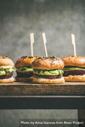 Upright fresh vegan burgers on seeded buns with skewer on wooden board bDELk0