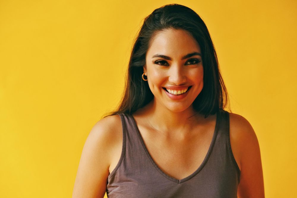 Headshot of happy Hispanic woman looking at camera with yellow background, copy space
