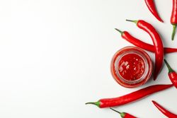 Glass jar with sauce and chilli pepper on blank background, top view