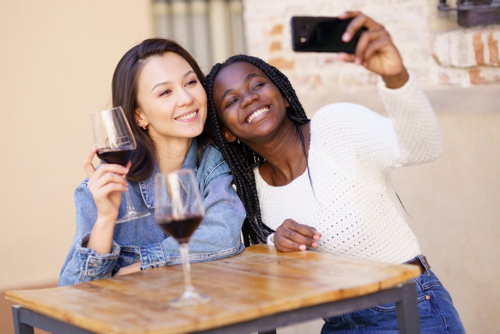 Female friends at a restaurant with glasses of red wine taking a self portrait