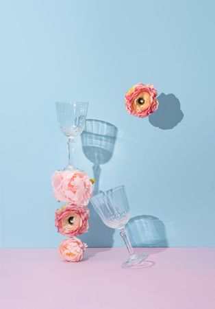 Wine glasses and flowers against a baby blue and pink background
