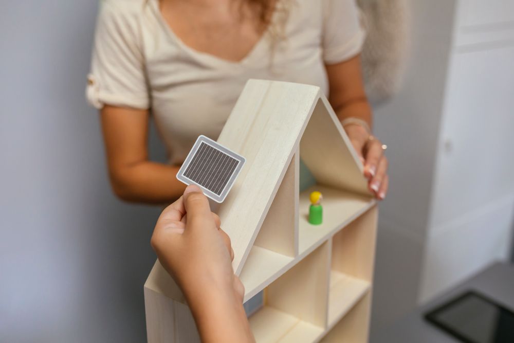 Unrecognizable student placing a solar panel on the roof of a toy house