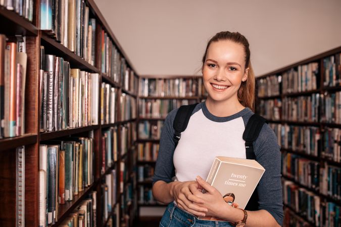 Young female student standing and holding book in university library