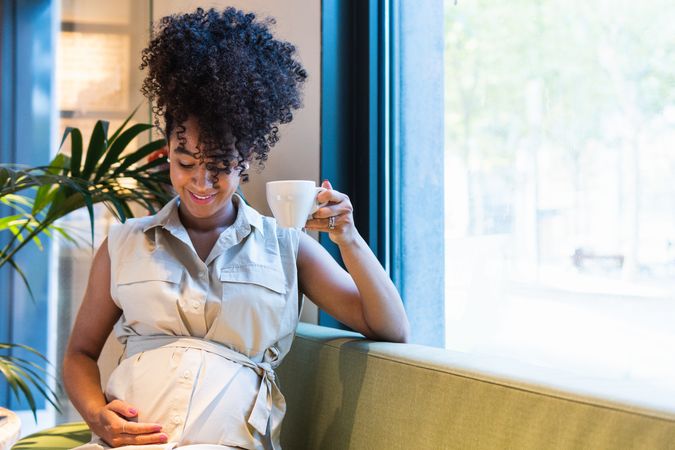 Smiling Black woman drinking coffee and touching tummy