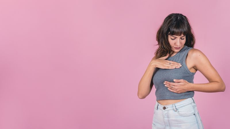 Woman doing a Breast Self-Exam over pink background. Copy space