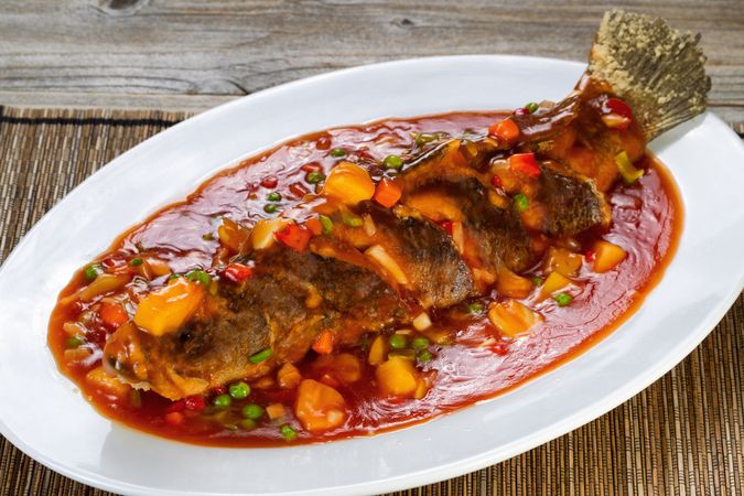 Fried whole fish in sauce with fruit and vegetables in serving plate ready to eat