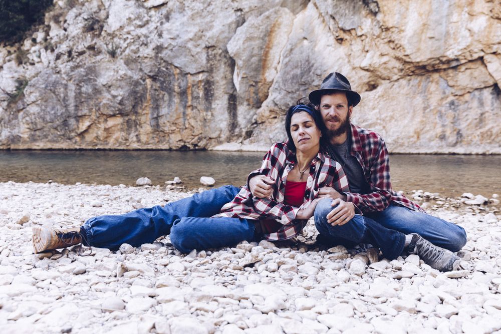 Positive woman and man resting on stone shore near river