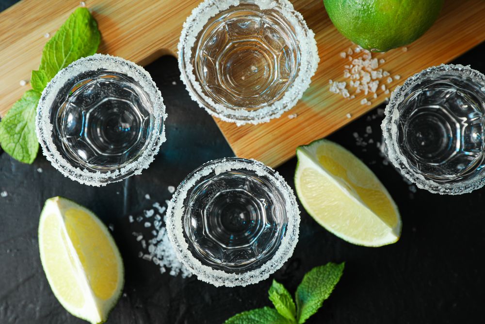 Tequila shots with salt, lime slices and mint on dark table