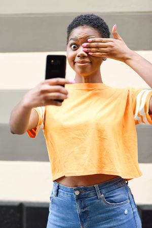 Female taking photo with one eye covered in front of striped wall, vertical composition