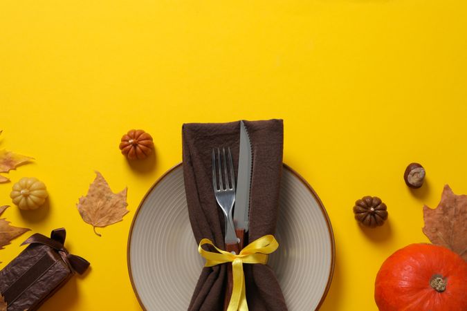 Cutlery on plate, leaves and pumpkins on yellow background, space for text