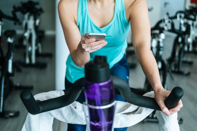 Woman with smartphone and towel and water on exercise machine