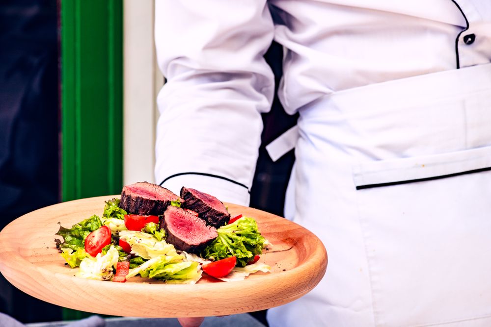 Waiter holding steak salad with fresh lettuce