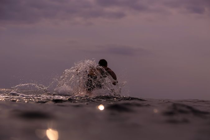 Man on surf board floating on water and cloudy sky