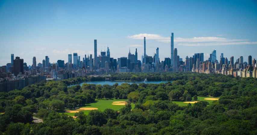 Aerial Helicopter Footage Over Central Park with Nature, Trees, People Having Picnic and Resting on a Field Around Manhattan Skyscrapers Cityscape. Beautiful Sunny Day. Slow Motion Footage