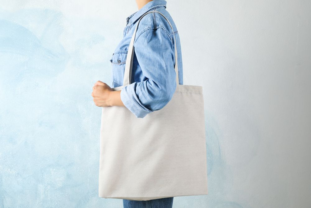 Young woman holding tote bag against blue background, empty space