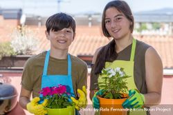 Portrait of two happy teenager wearing gardener apron posing with plants on balcony 4d8aZE