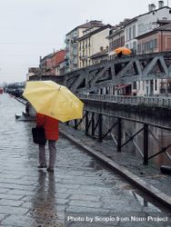 Person in red coat holding yellow umbrella walking on sidewalk bGBzl4