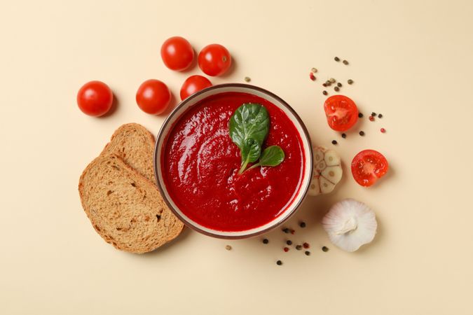 Top view of bowl of tomato soup with ingredients and slices of bread