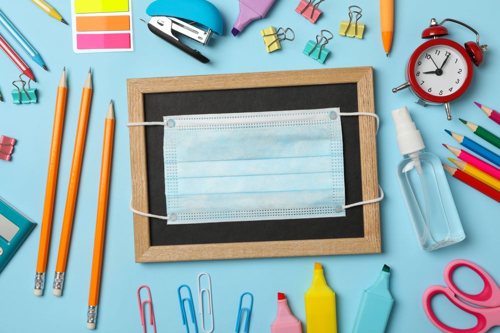 School supplies with medical mask and sanitizer on blue background