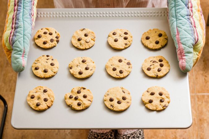 Woman holding a tray with baked cookies with kitchen gloves
