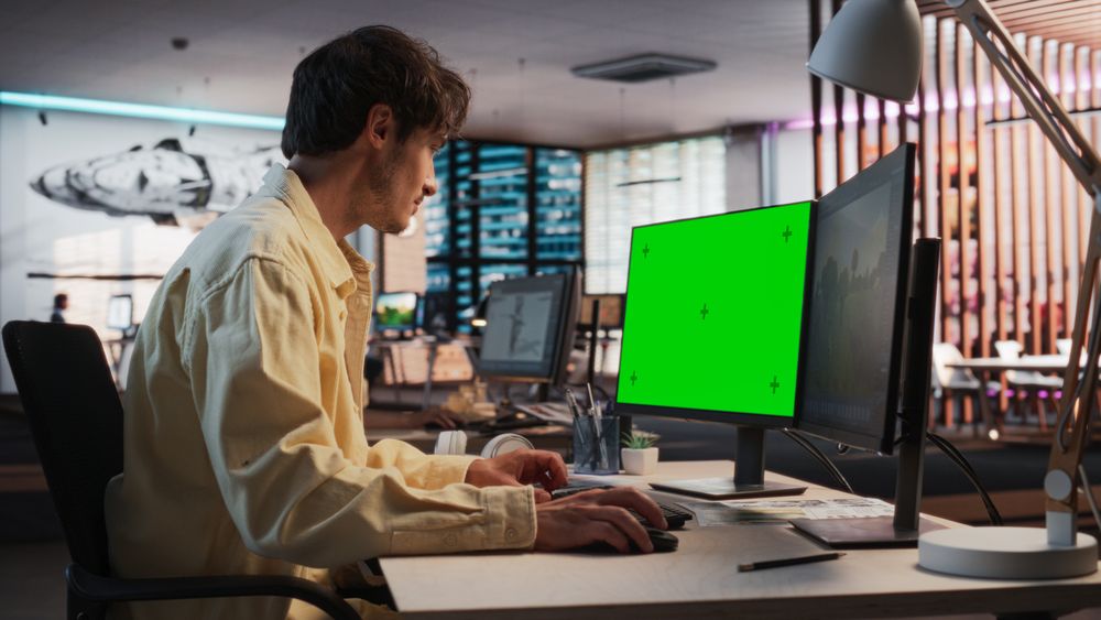 Portrait of Creative Man Sitting at a Desk Using Desktop Computer with Mock-up Green Screen Chromakey.