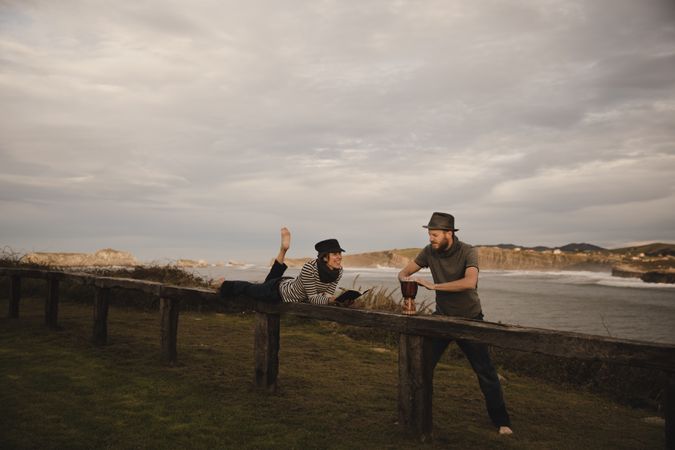 Man plying on drum near woman with notebook on bench on shore