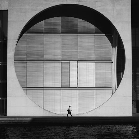 Grayscale photo of a man walking beside a building
