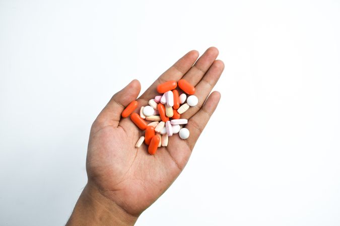 Variety of colorful medication and vitamins in hand with plain background
