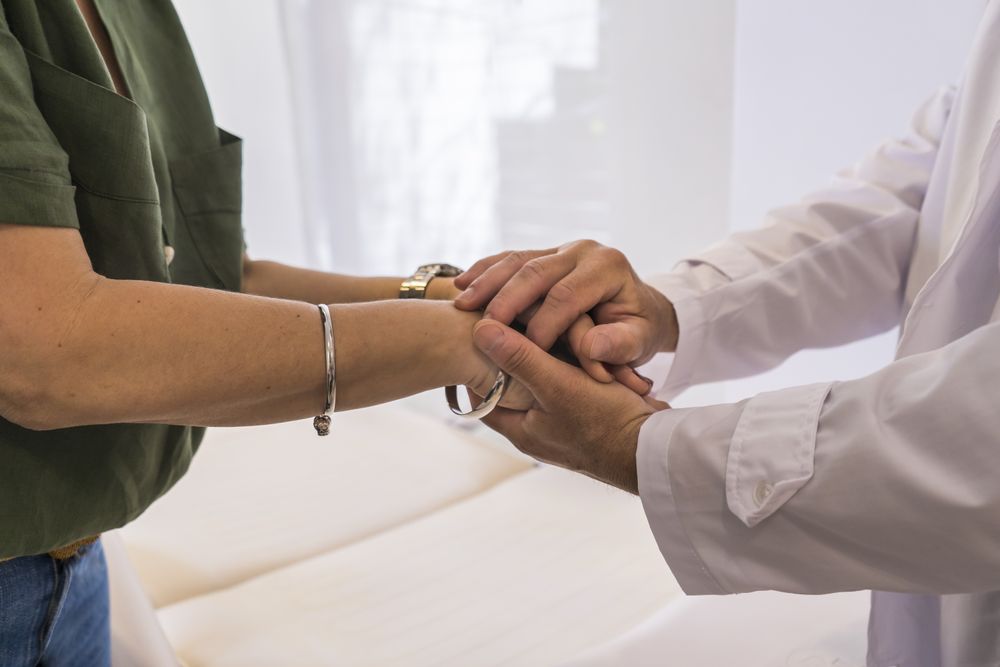 Male doctor holding hands with his female patient at the hospital.