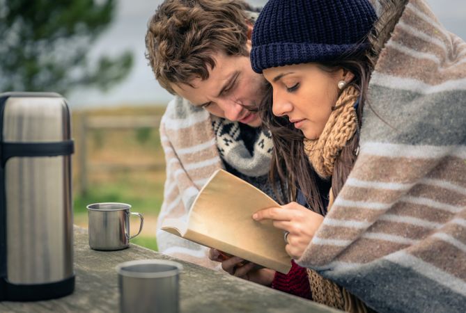 Couple sitting on park bench and making plans with flask of coffee on cold autumn day