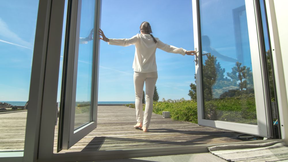 Shot of a Brunette with Loose Hair Opening Doors of the Balcony and Walking onto Sunny Terrace with Seaside View.