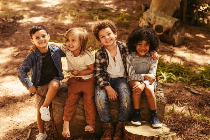 Group of four kids sitting on a wooden log outdoors